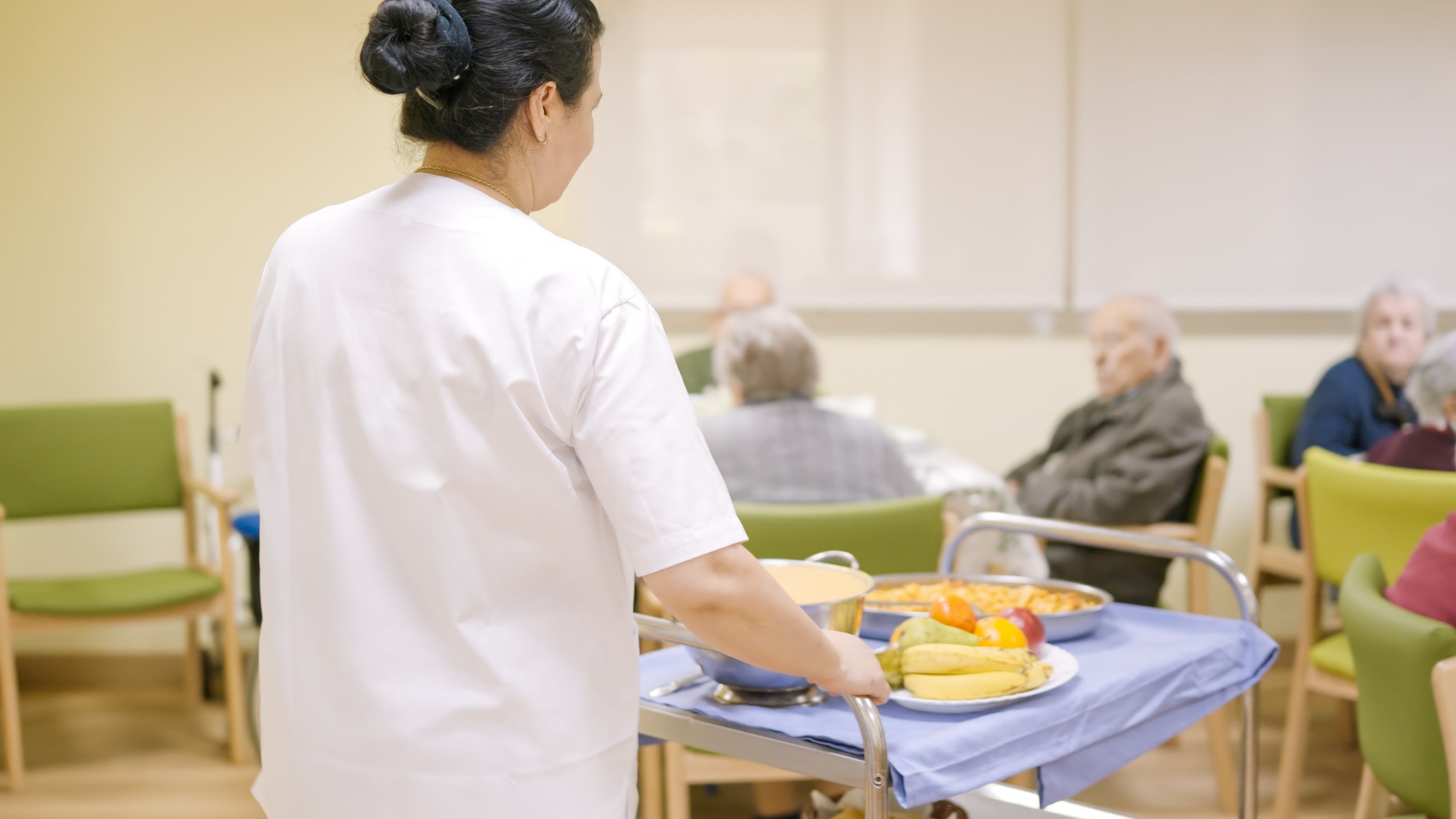 Aged Care worker walking with food cart into dining area