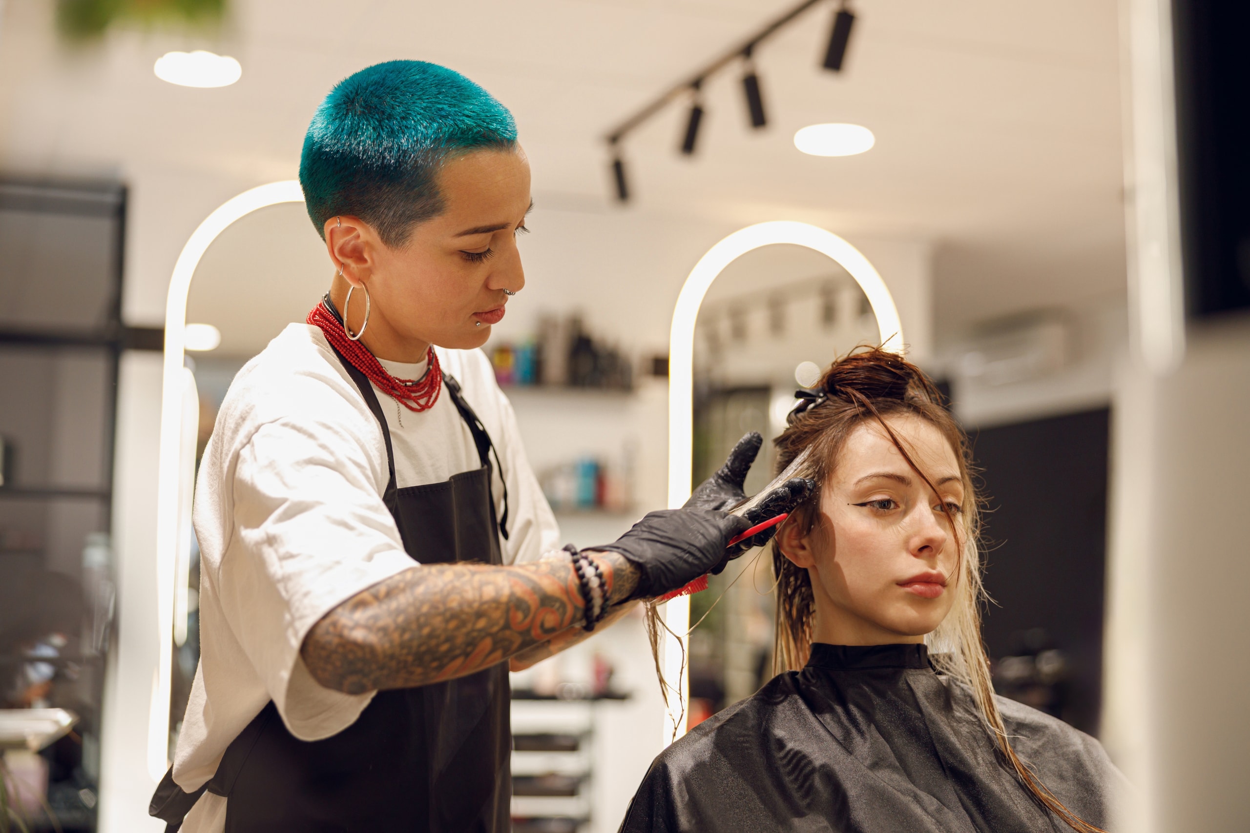 Female hairdresser is dying hair of client with brush while working in professional salon