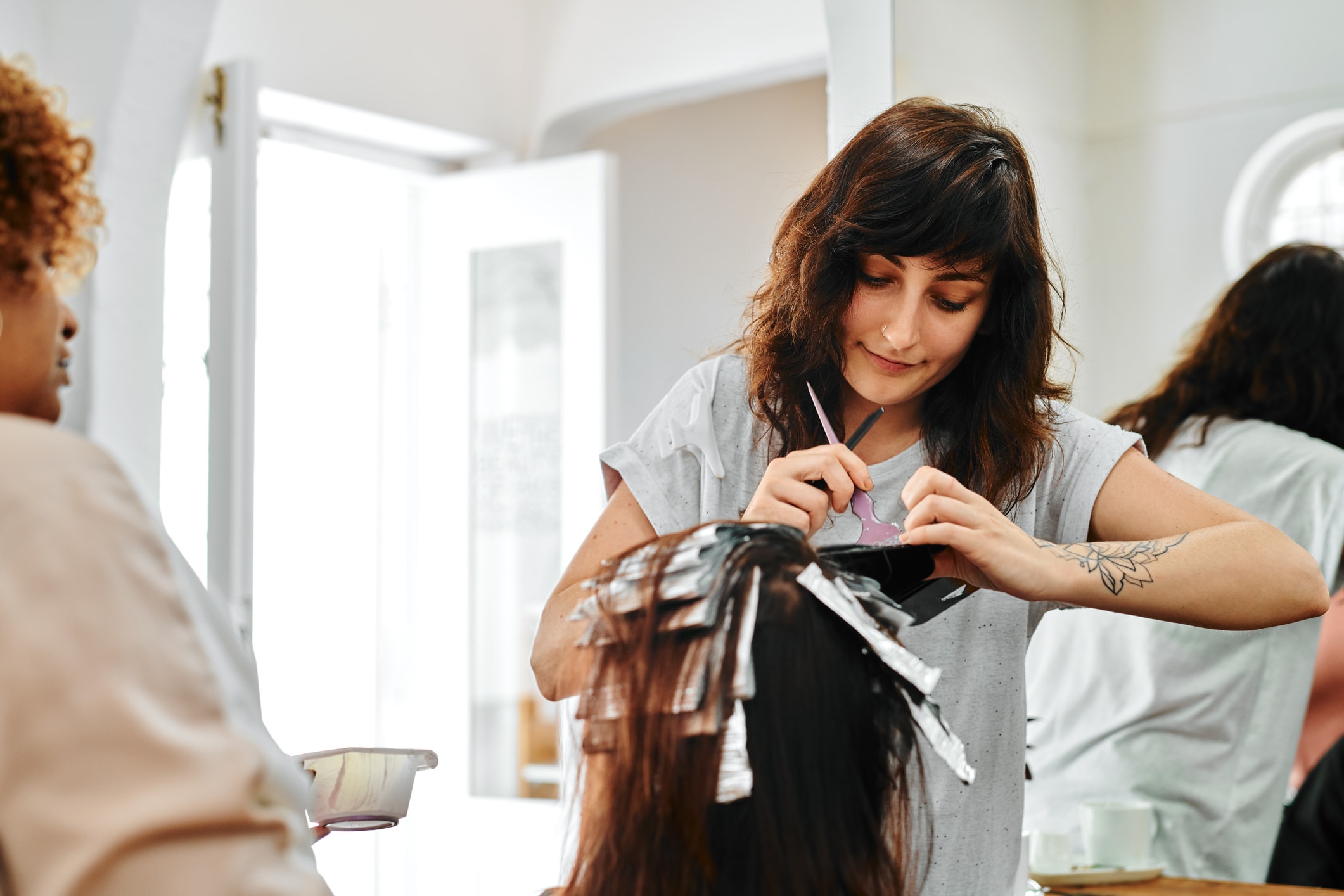 Cropped shot of two young hairdressers standing and applying hair dye to their client's hair in a salon